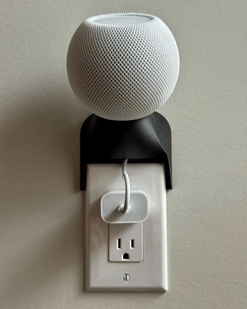 HomePod mini installed above a wall outlet on the black SPEKURA outlet mount