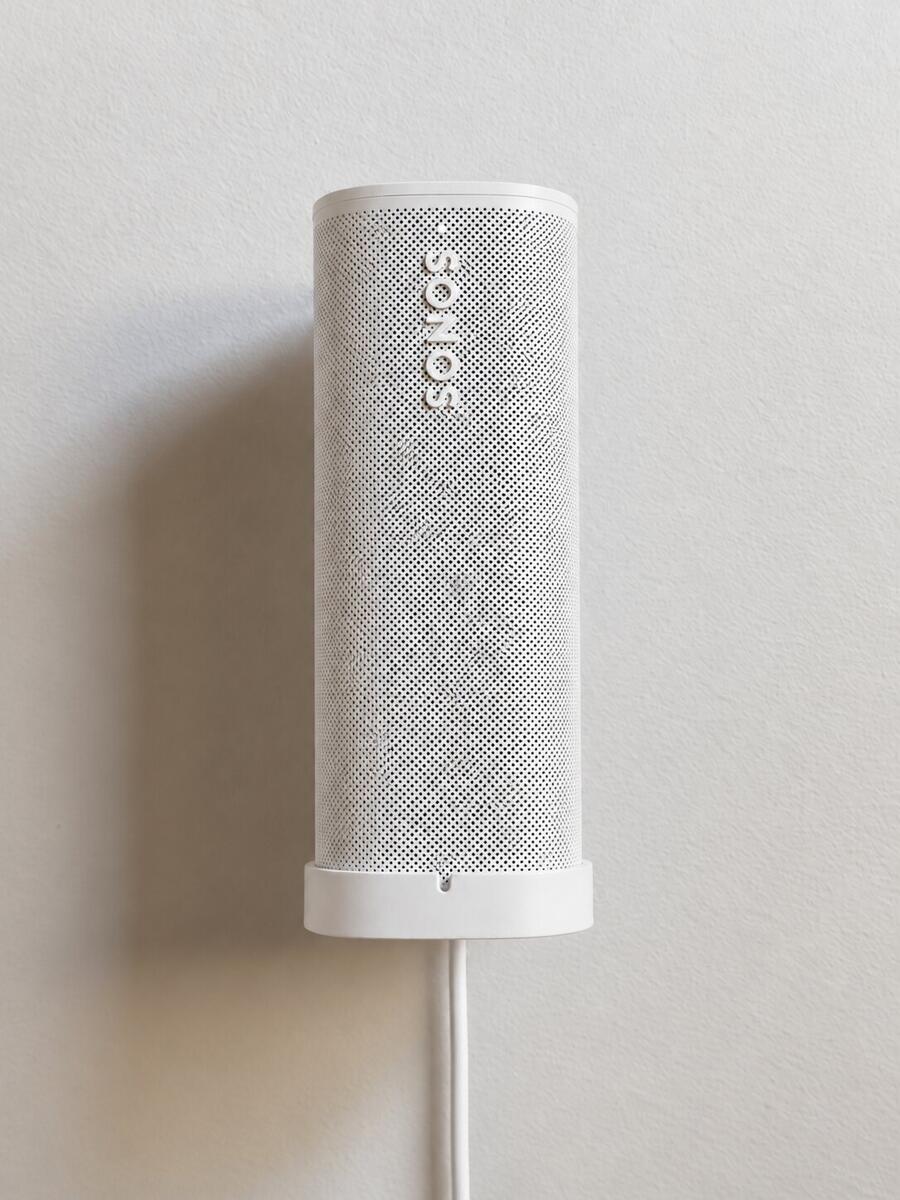 White Sonos Roam installed vertically on the white SPEKURA cable wall mount with a white charging cable