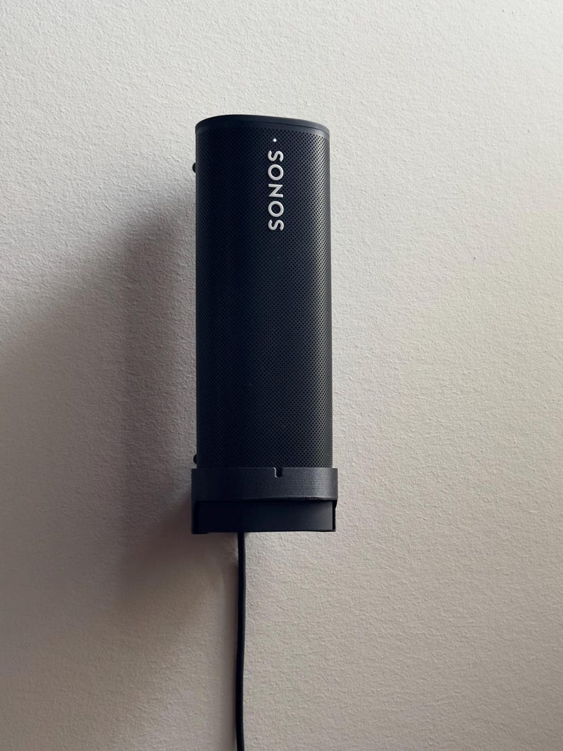Black Sonos Roam seated on the black SPEKURA wall mount with the official wireless charger